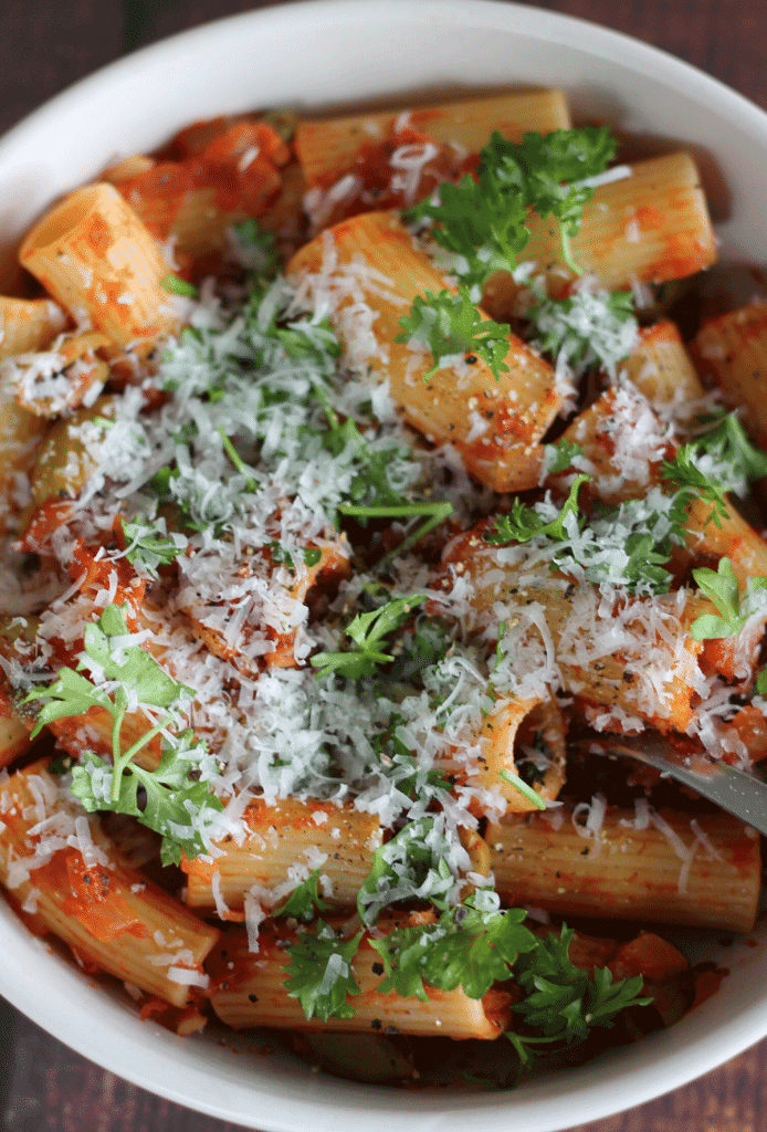 A bowl of puttanesca rigatoni with parmesan and parsley