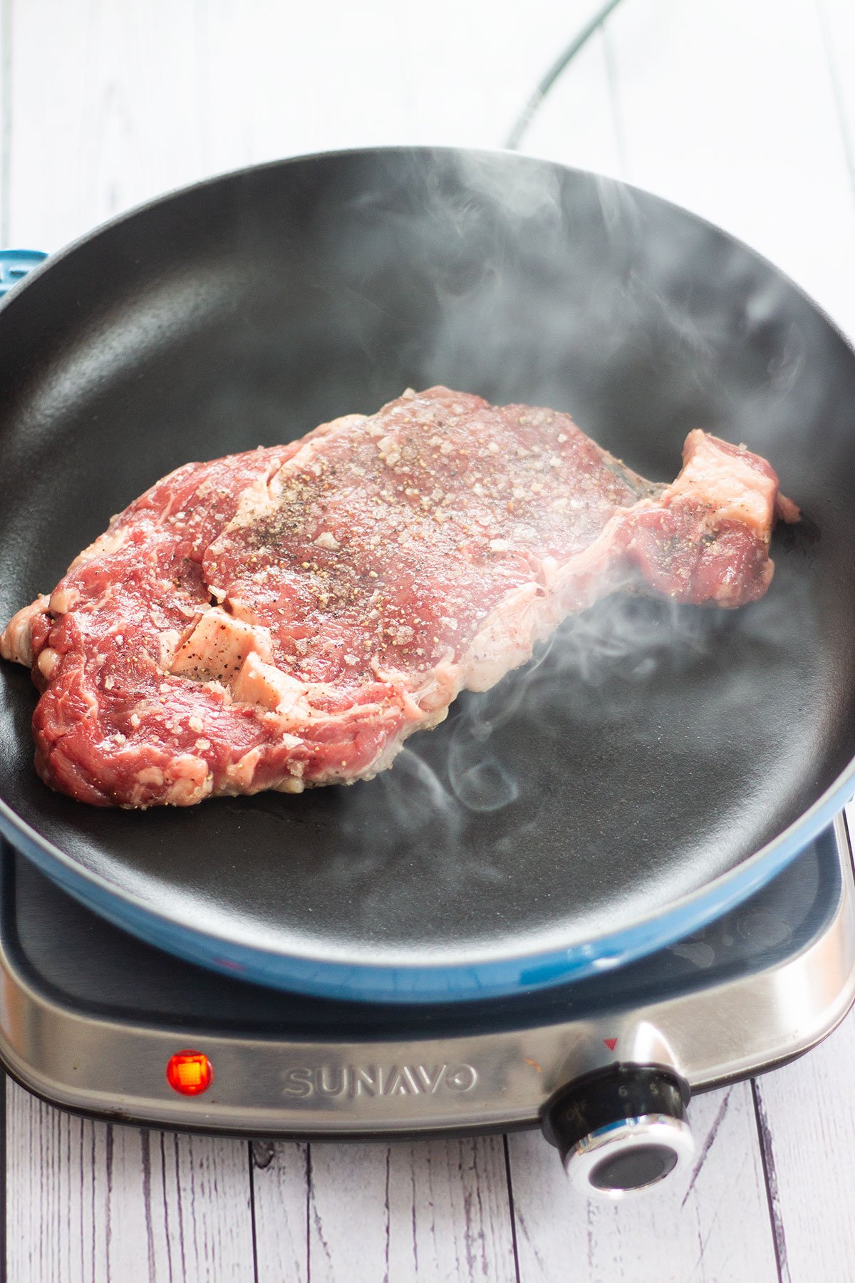 ribeye steak being seared in a pan