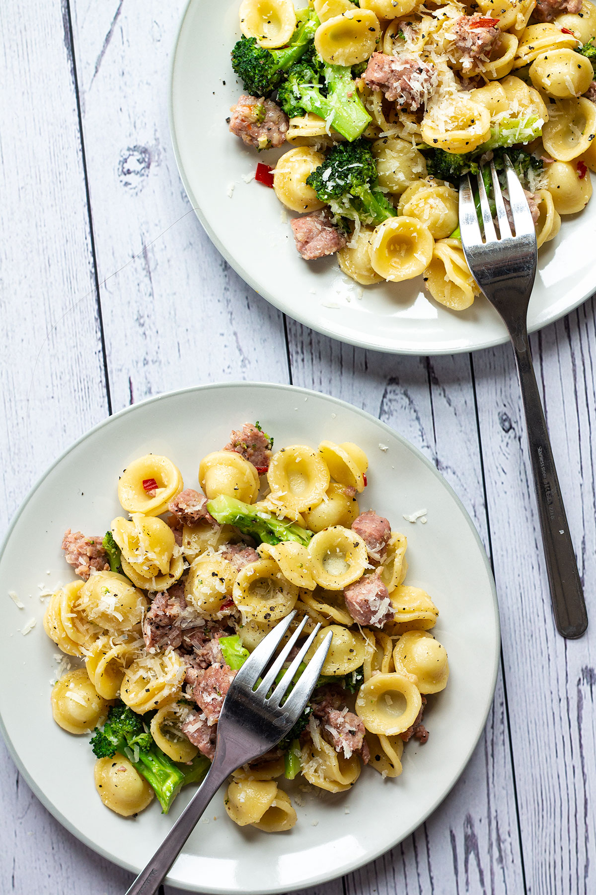 Two plates of broccoli and sausage pasta.