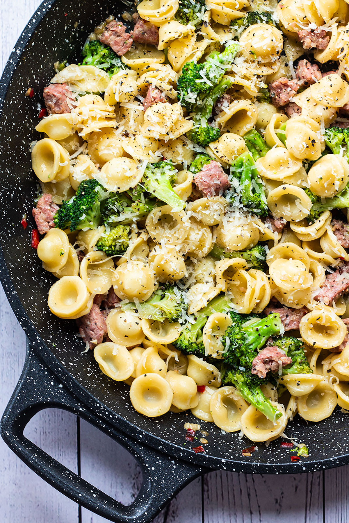 Broccoli and sausage pasta in a pan topped with Parmesan.