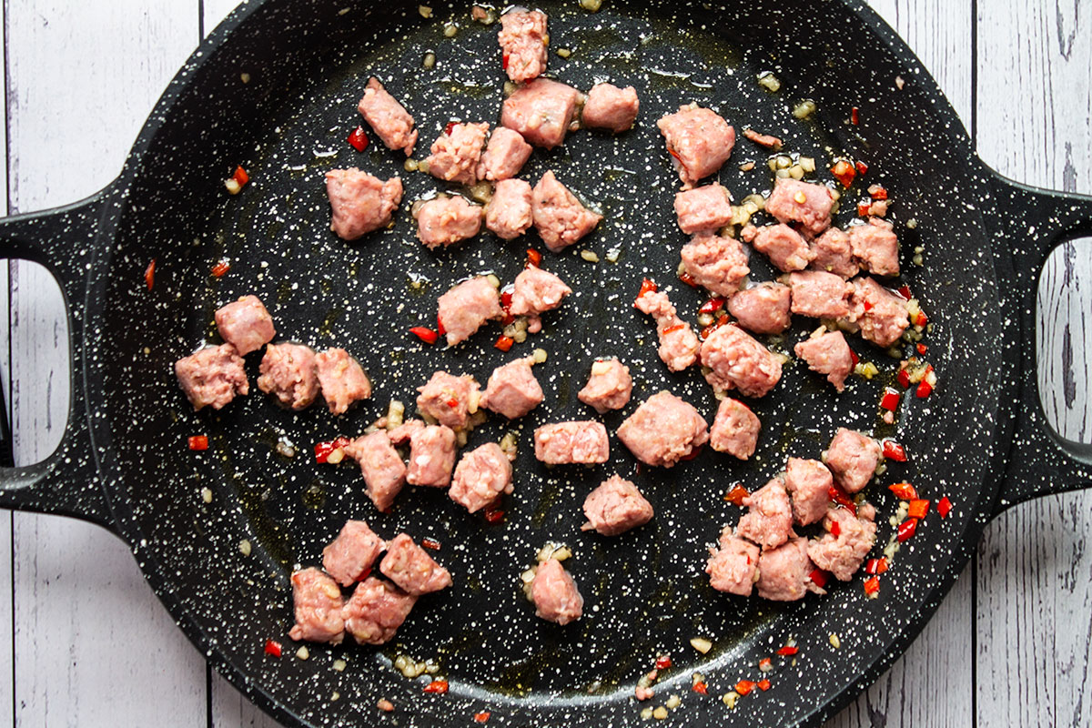 Sausage pieces being fryed in a black pan. 
