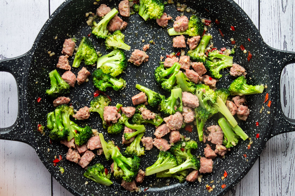 Broccoli and sausage in a black pan.
