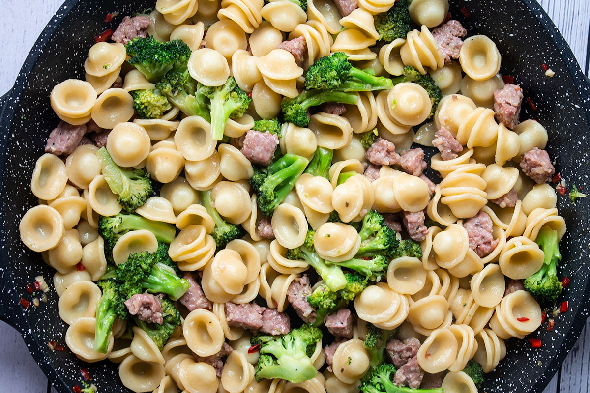 A pan of cooked broccoli and sausage with orecchiette pasta. 