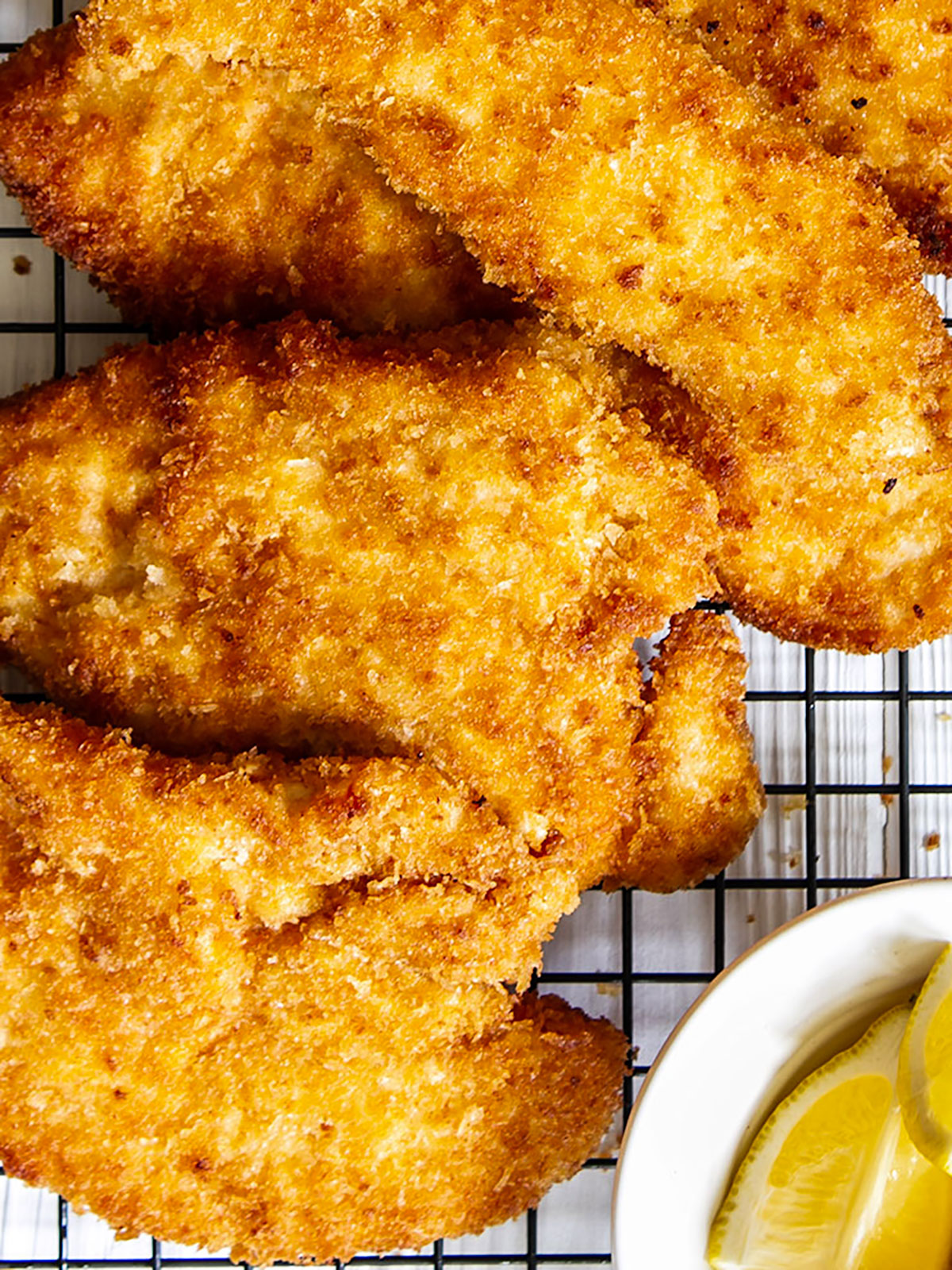 Panko chicken on wire rack with lemon wedges.
