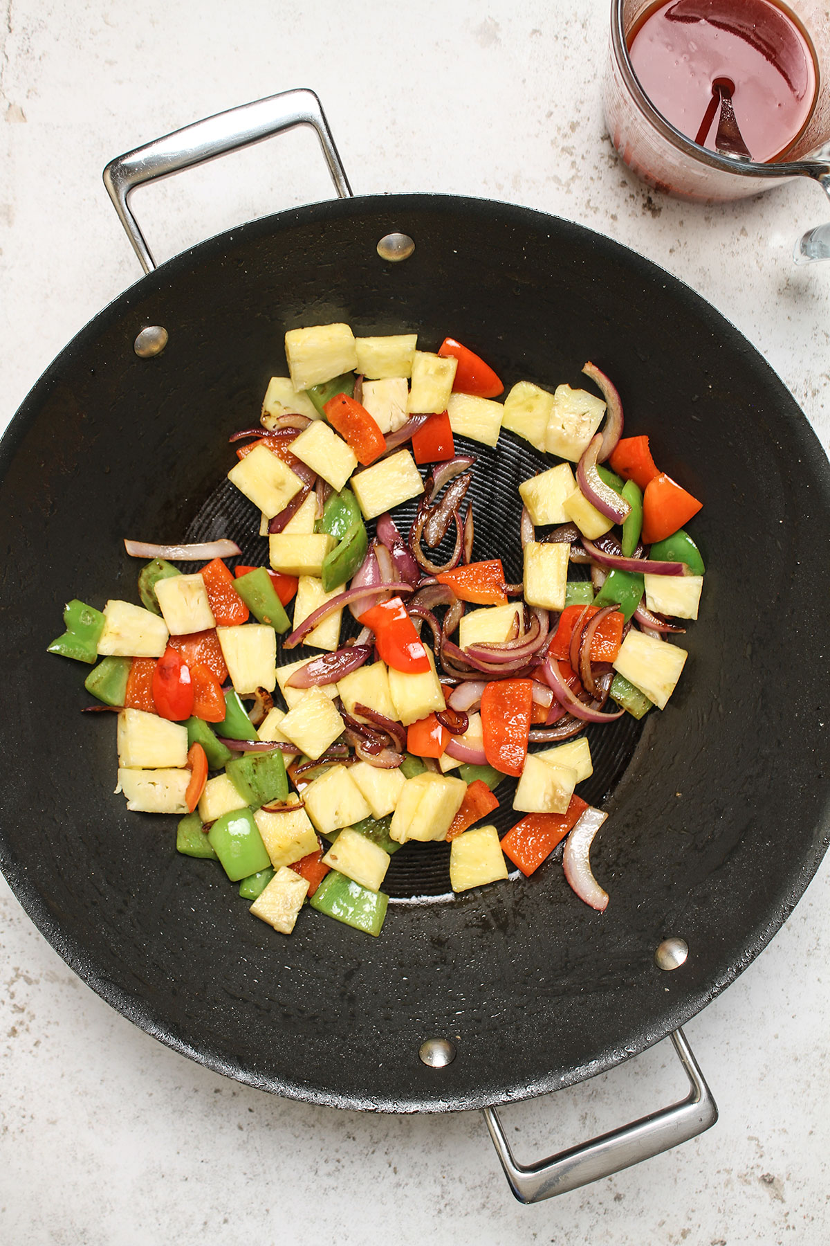 Onions, pepper and pineapple in a wok.