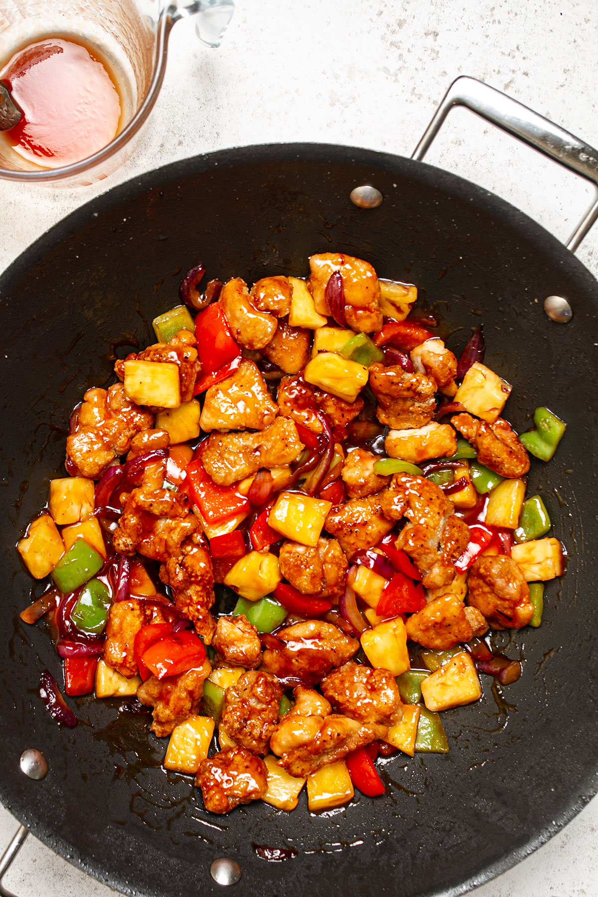 A wok containing the cooked veggies and fried chicken coated in the sweet and sour sauce.