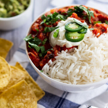 a bowl of chilli served with guacamole and tortilla chips