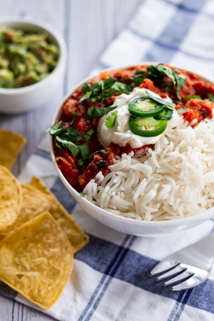 a bowl of chilli served with guacamole and tortilla chips