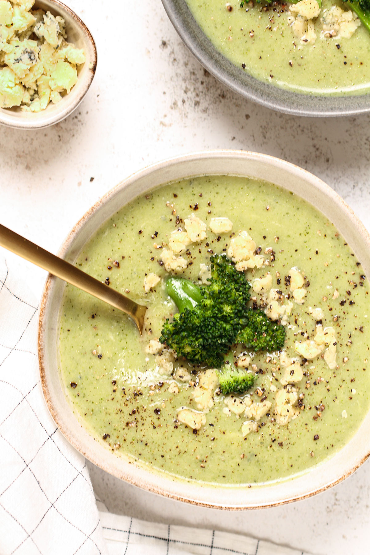 Two bowls of broccoli and stilton soup topped with crumbled stilton.