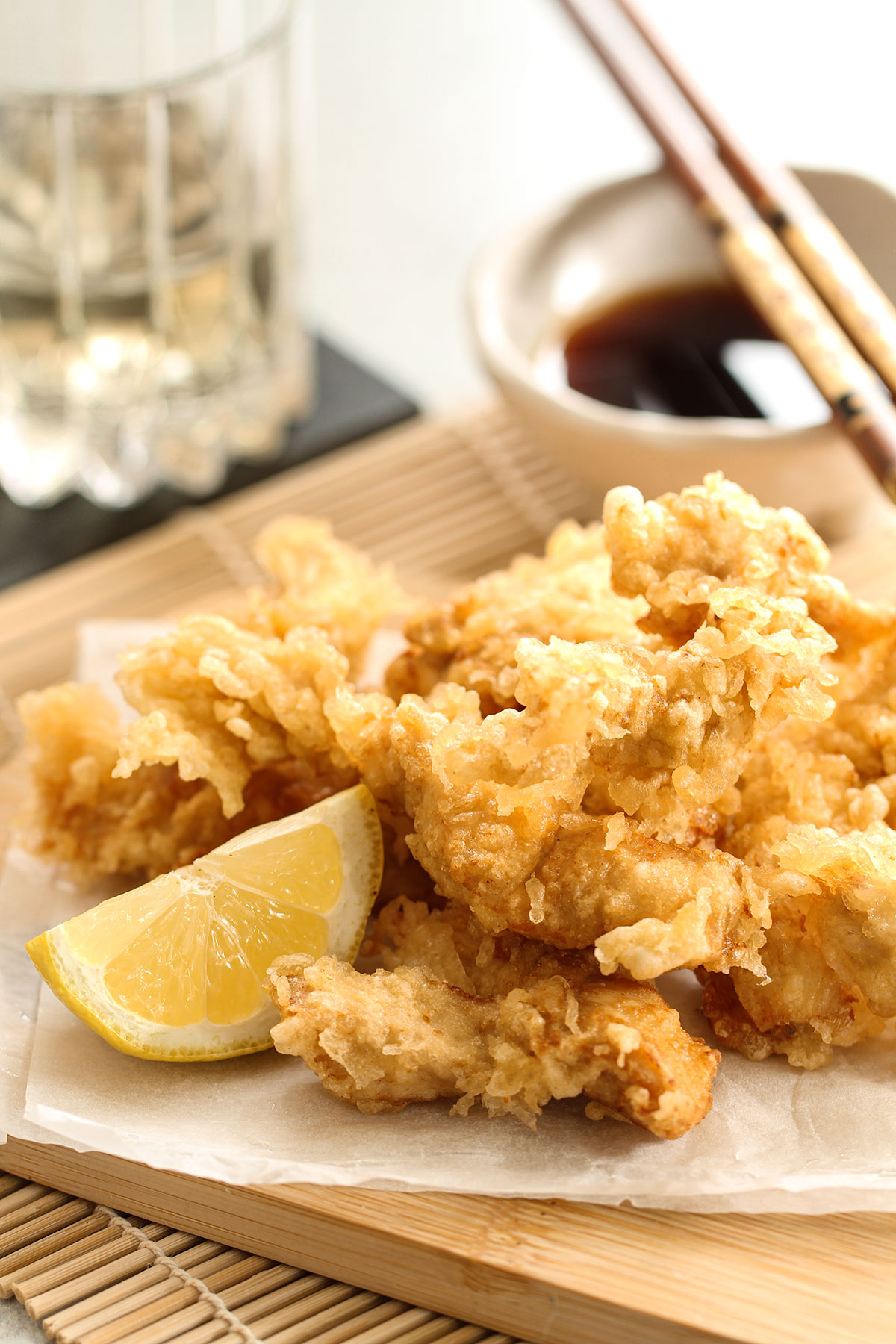Chicken Tempura with a slice of lemon on a wooden board with a bowl of ponzu dipping sauce and chopsticks in the background.