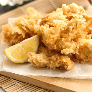Close up of Chicken Tempura with a slice of lemon on a wooden board.