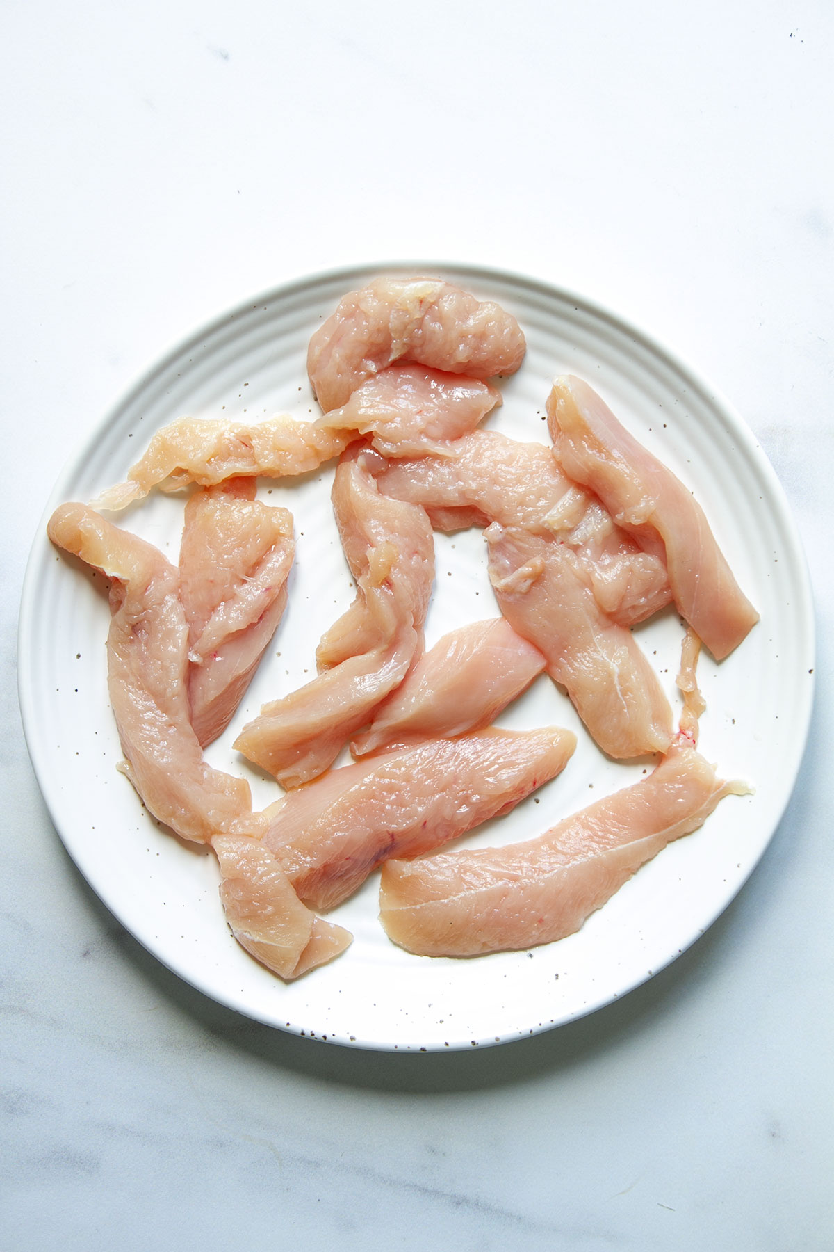 Tenderised chicken pieces on a white place.