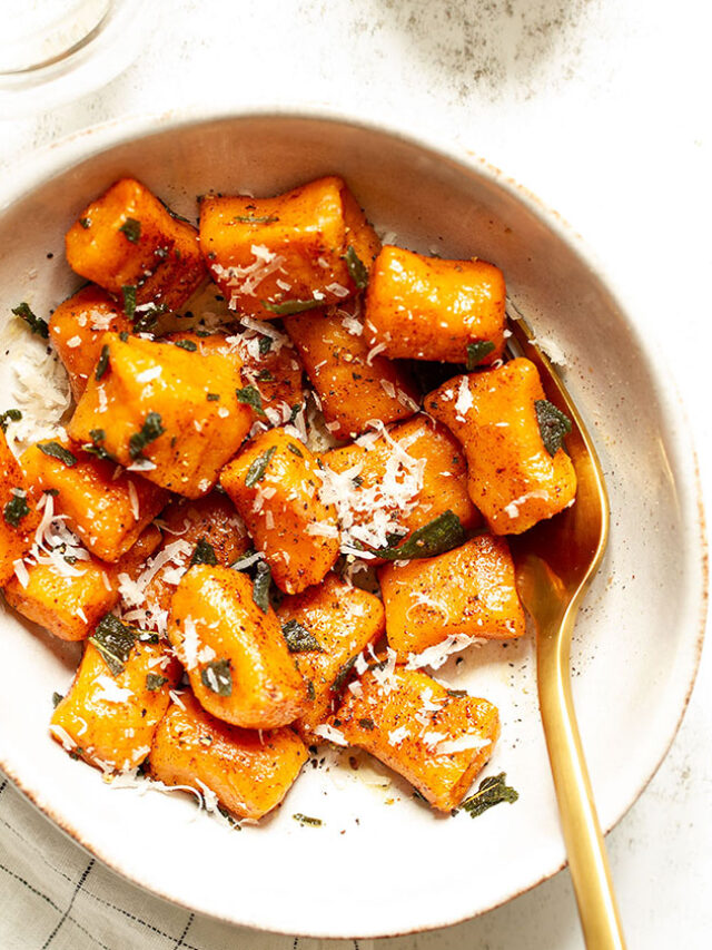 A bowl of sweet potato gnocchi with a fork on a white background.