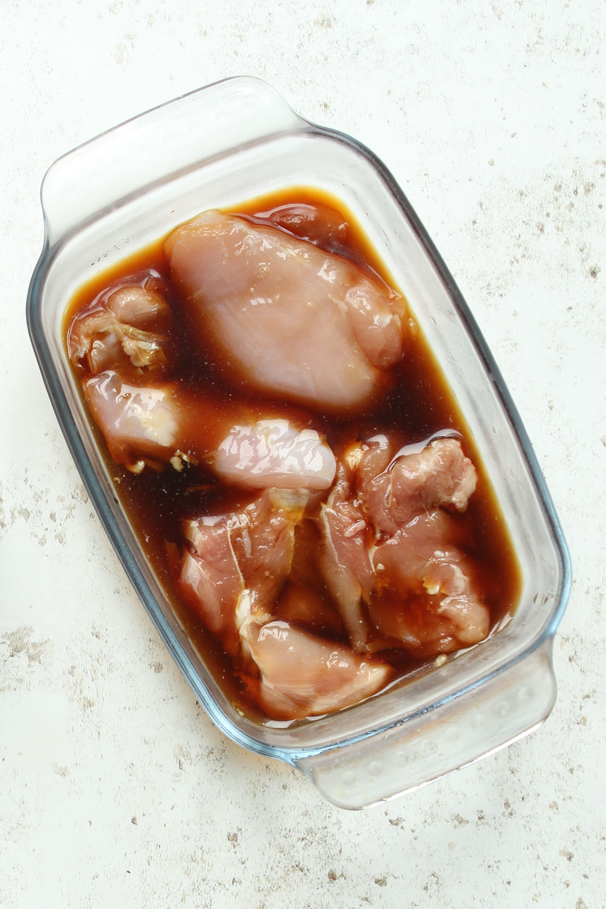 Chicken thighs marinating in a glass dish.