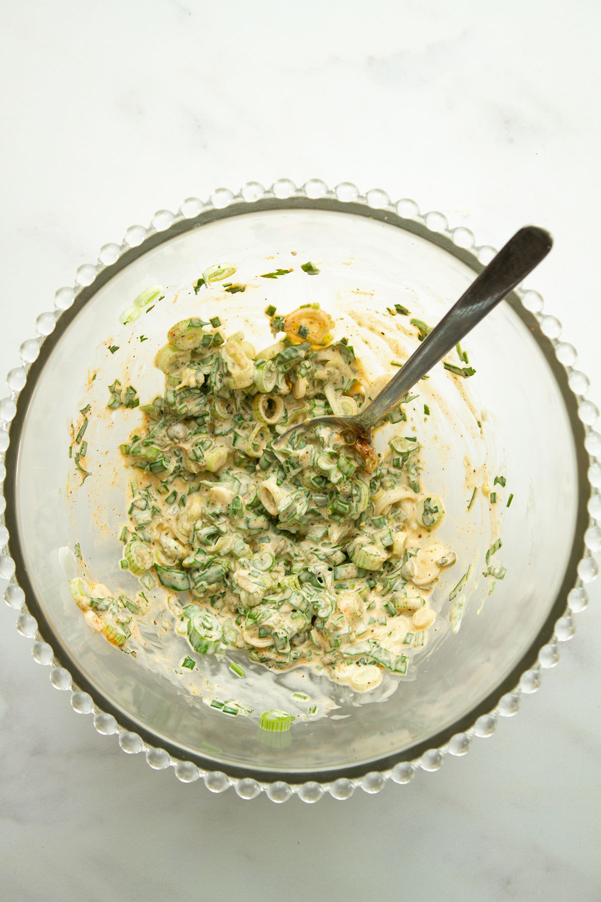 The dressing with scallions capers, parsley, and chives in a glass bowl.