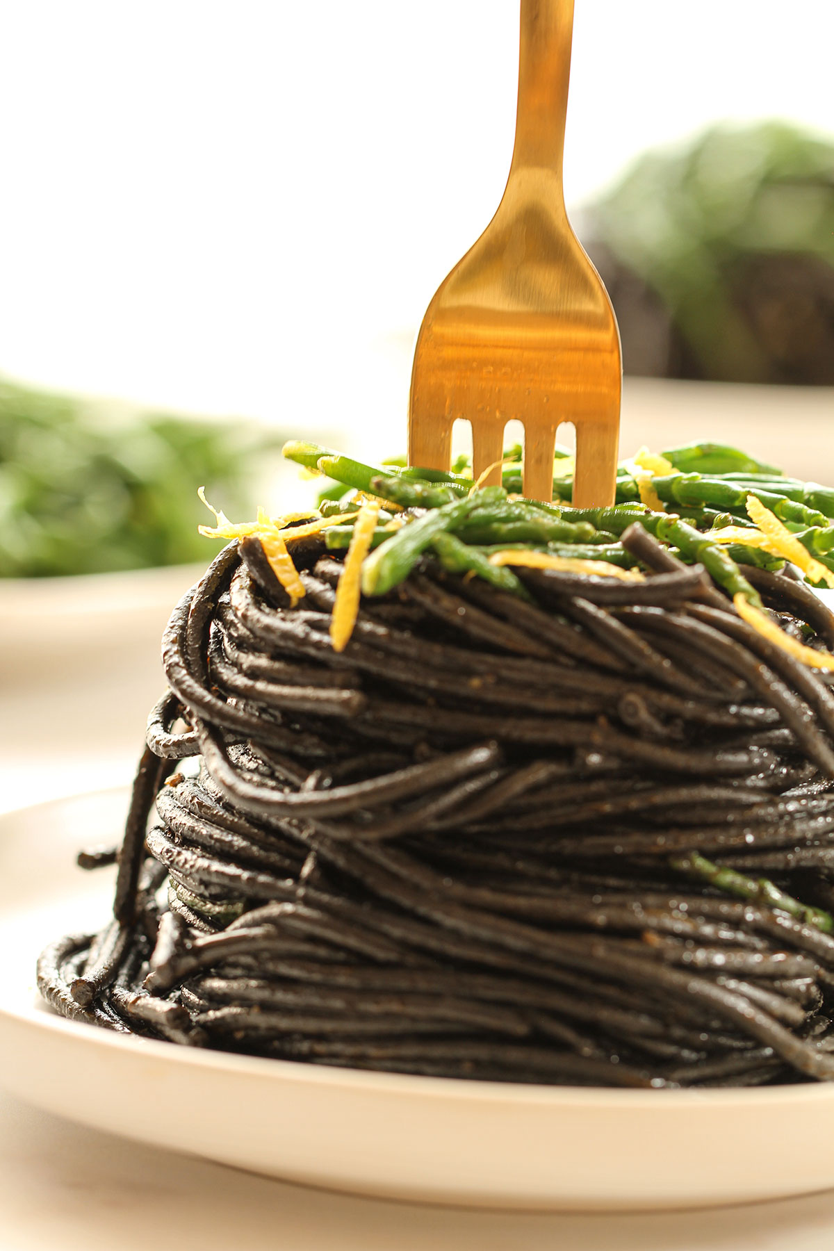 Close up of a plate of black squid ink pasta topped with samphire and lemon zest.