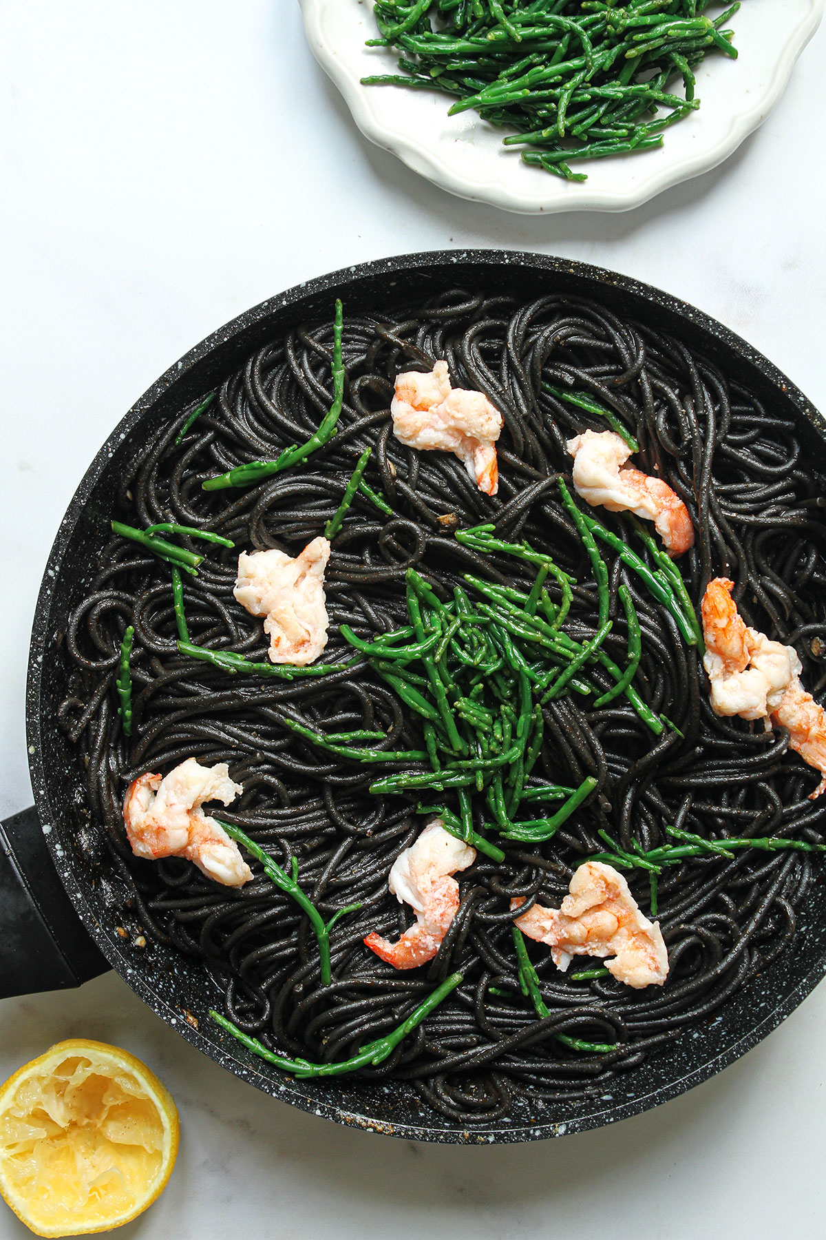 The cooked squid ink pasta served with cooked prawns, samphire and lemon juice with a plate of samphire and a squeezed half lemon.