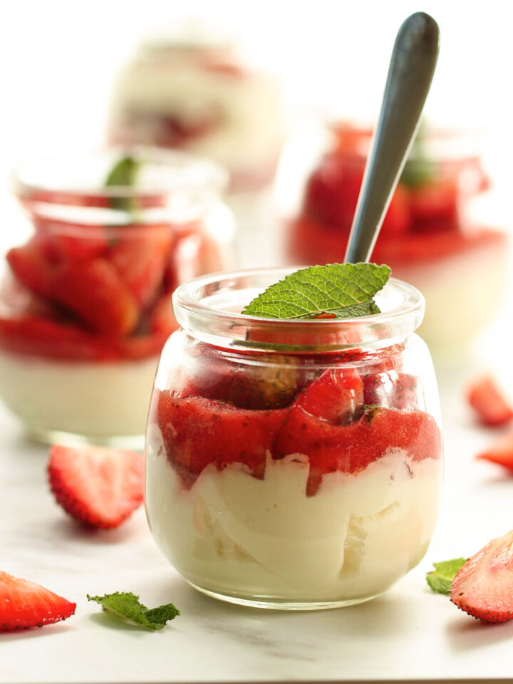 A dessert jar of strawberries and cream with a mint leaf topping.