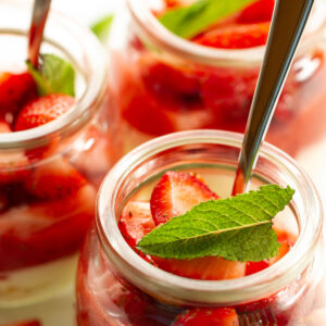 A dessert jar of strawberries and cream with a mint leaf topping.
