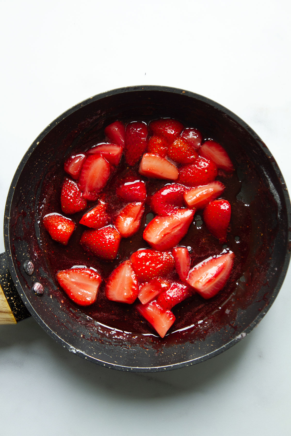 A frying pan containing the strawberrries which are being heated until softened.