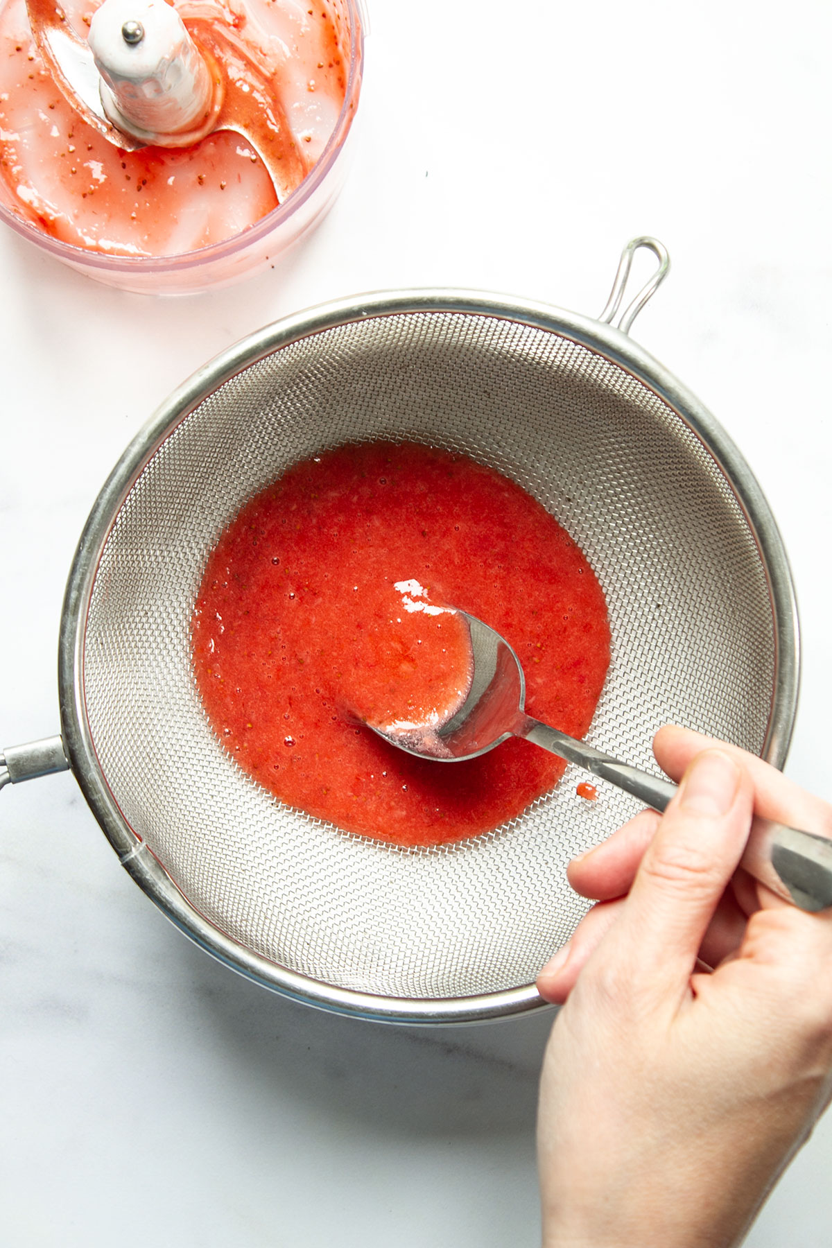 The blended mixture of strawberries, icing sugar and lemon juice being strained through a sieve.