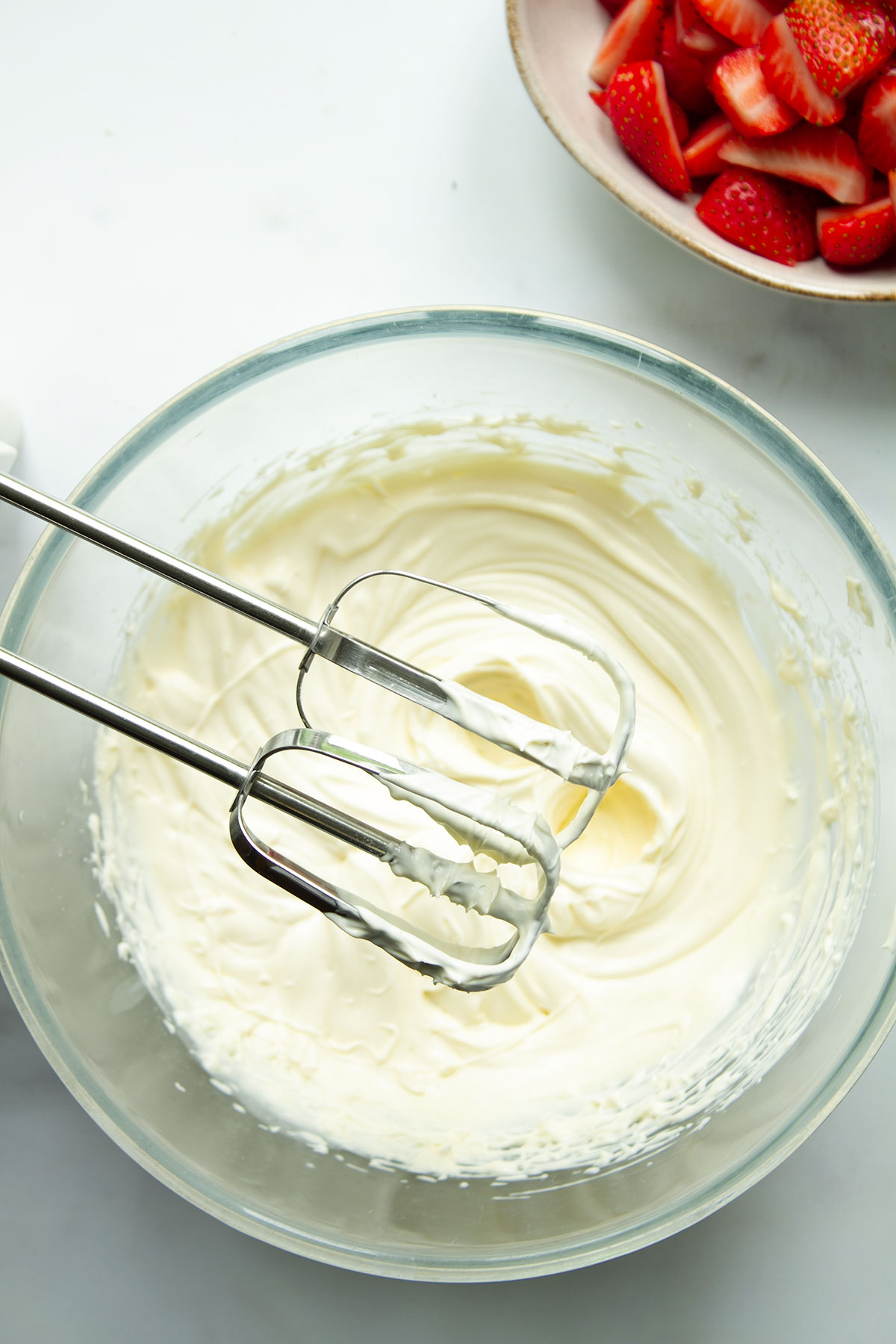 A bowl of cream, icing sugar and vanilla essence being whisked until stiff peaks start to form.