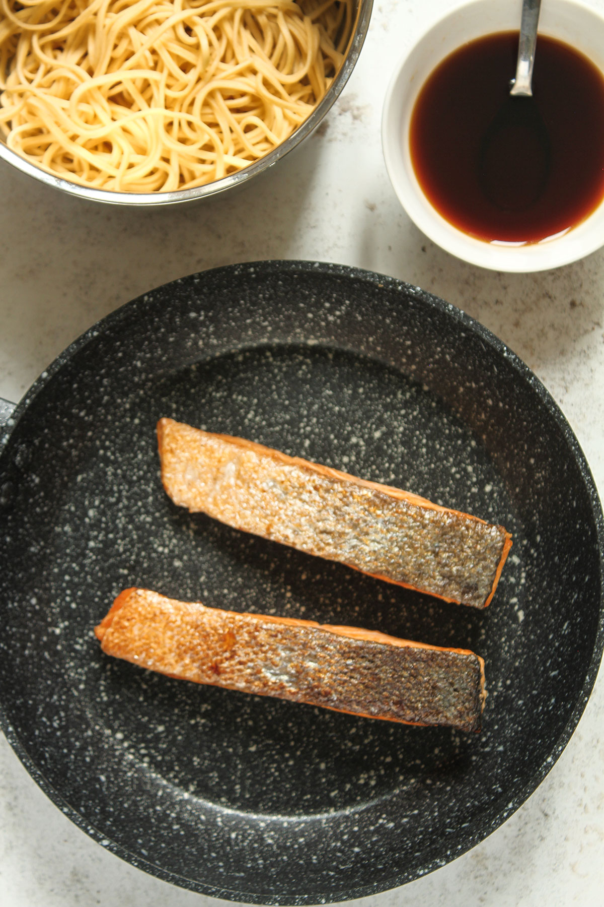 Two cooked salmon fillets in a frying pan on a white background.