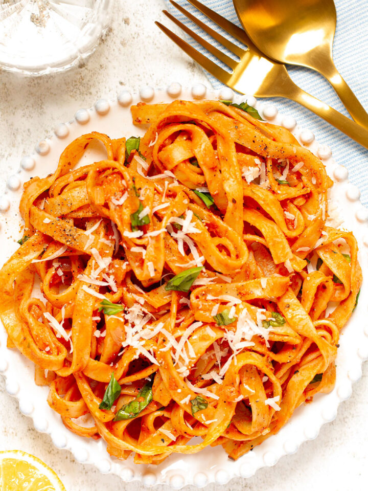 A bowl of Mascarpone Tomato Pasta on a white background with cutlery and a side of half a lemon.