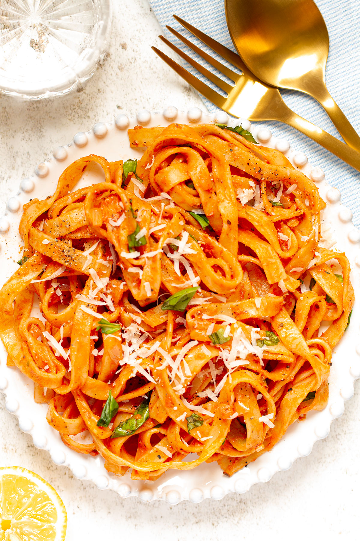 A bowl of Mascarpone Tomato Pasta on a white background with cutlery and a side of half a lemon.