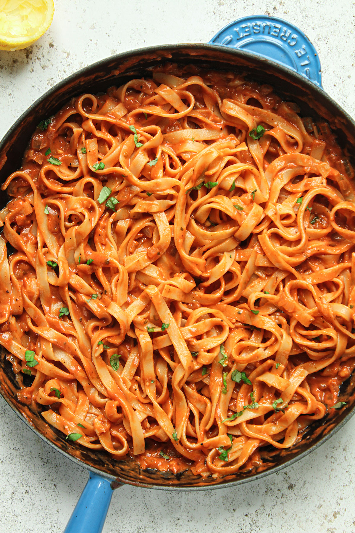 The cooked pasta with added passata sauce in a frying pan on a white background.