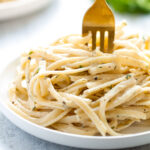 A bowl of pasta with creamy white wine sauce on a pale blue background.