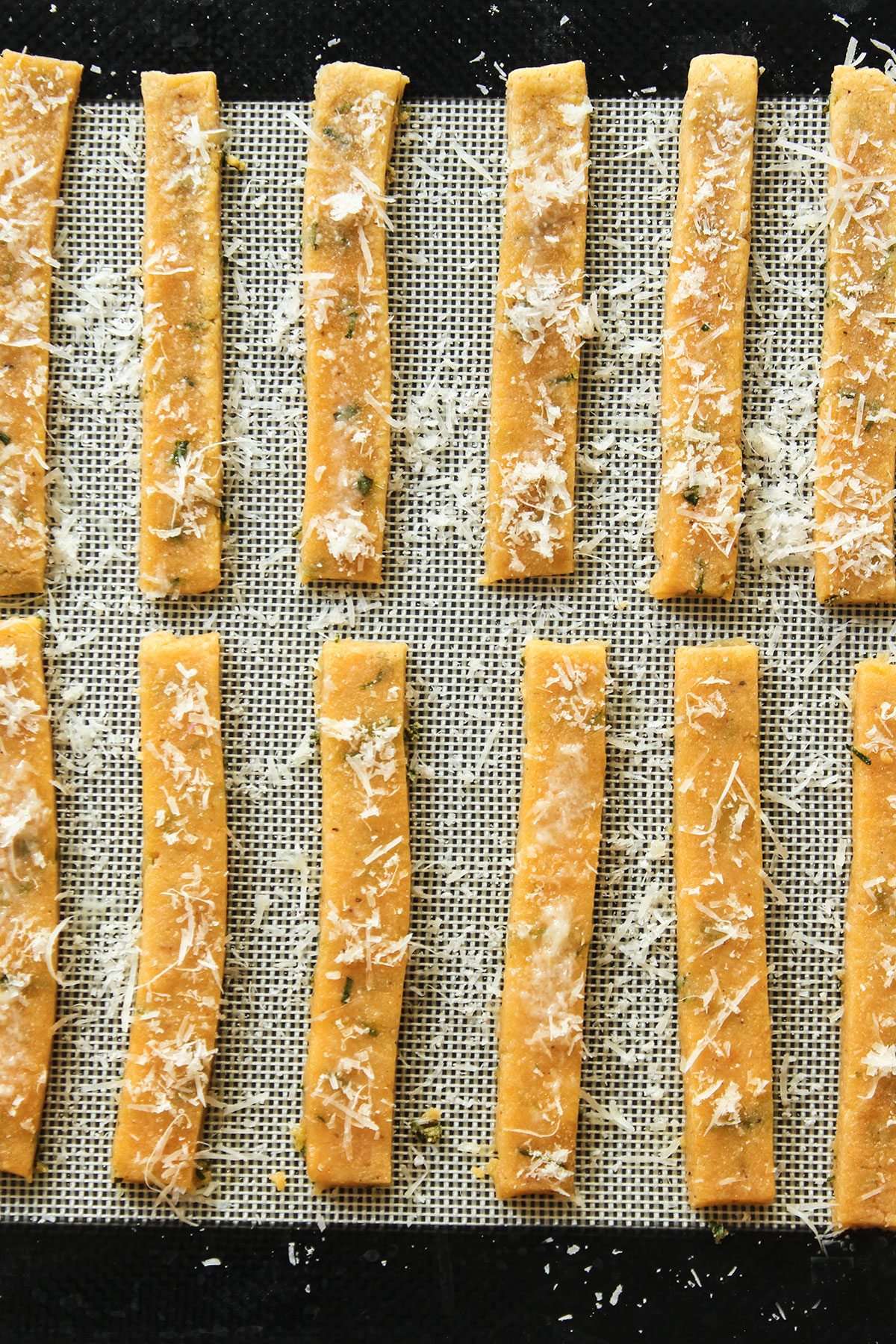 The dough strips brushed with egg white and sprinkled with Parmesan on a gauze background.