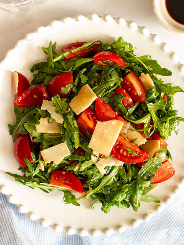 Rocket salad with tomatoes and Parmesan shavings on a white plate.