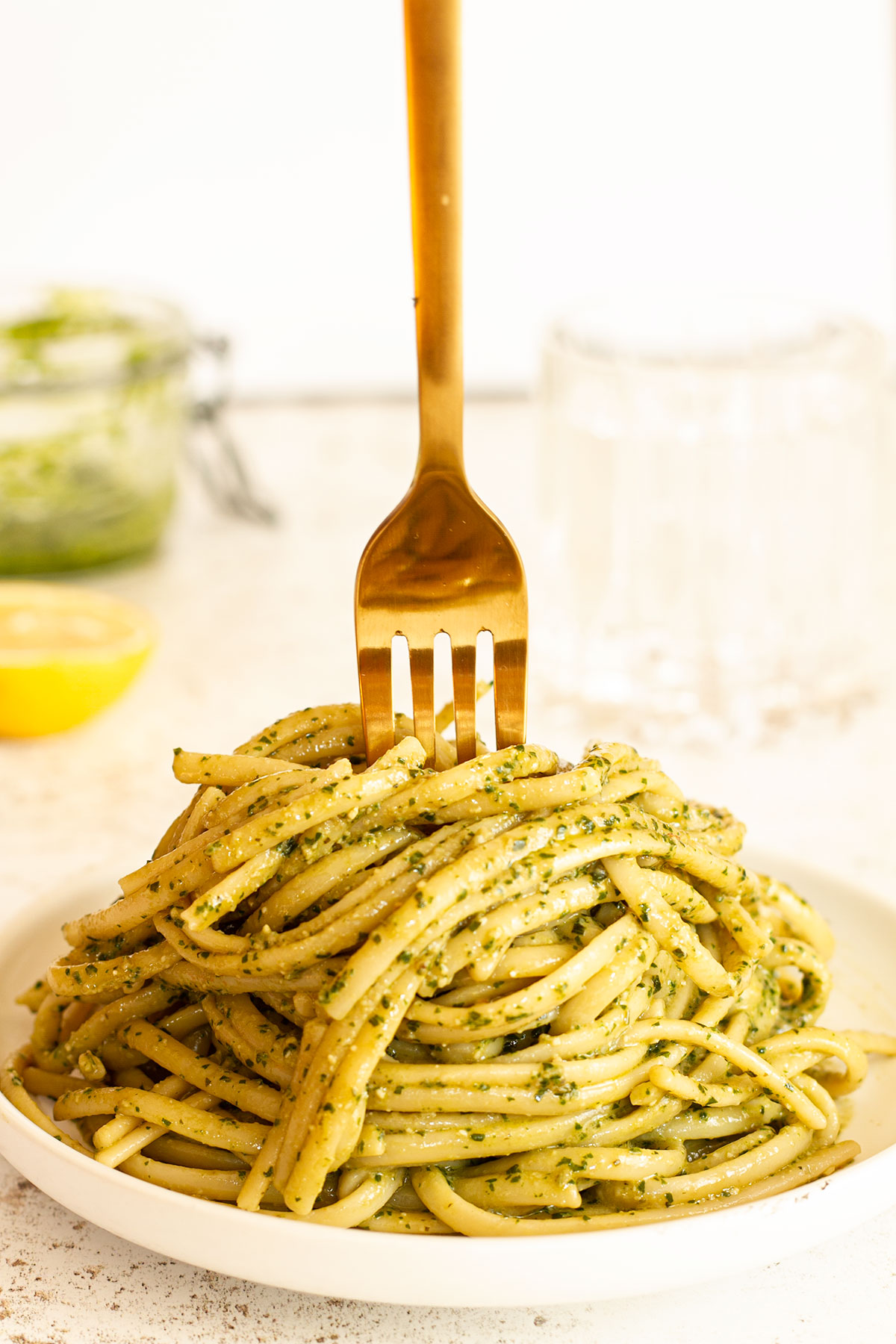 Pesto pasta served on a white plate with a half lemon in the background.