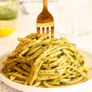 Pesto pasta served on a white plate with a half lemon in the background.