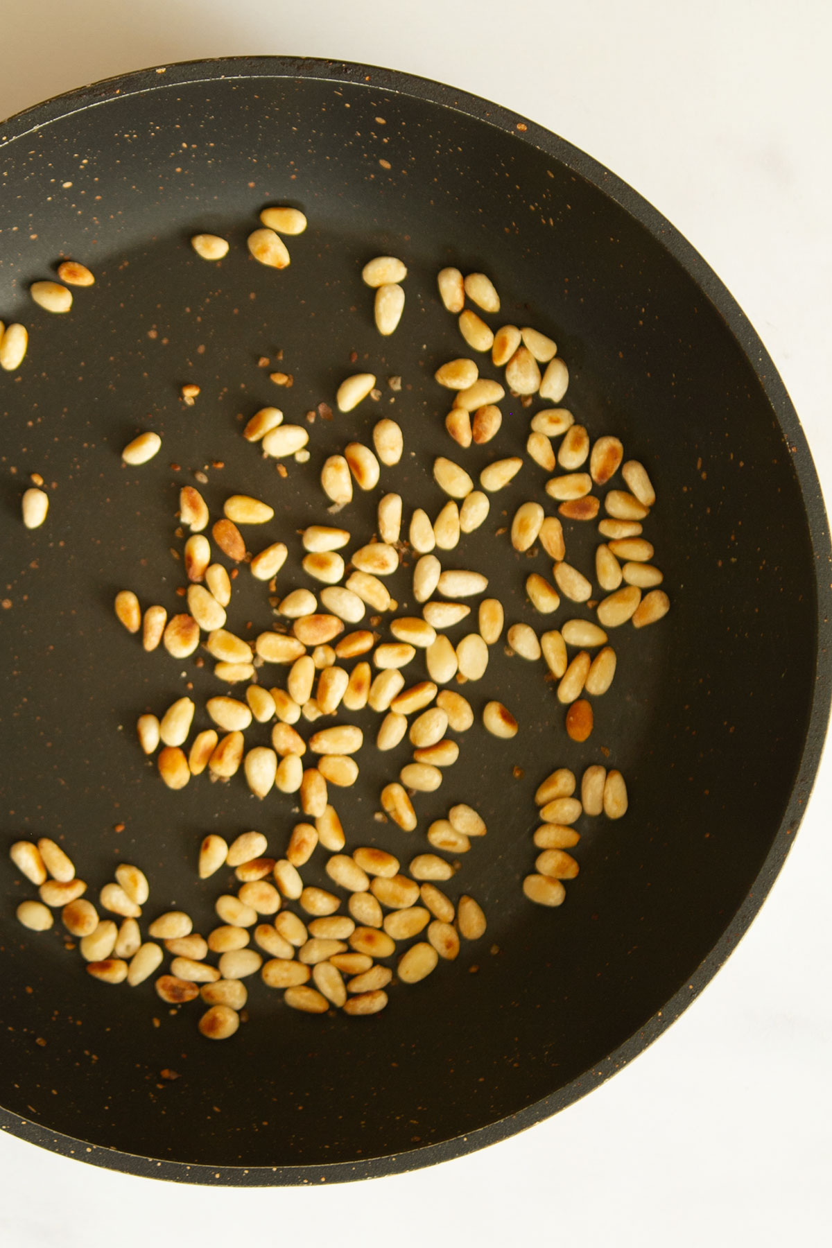 Toasted pine nuts in a black pan.