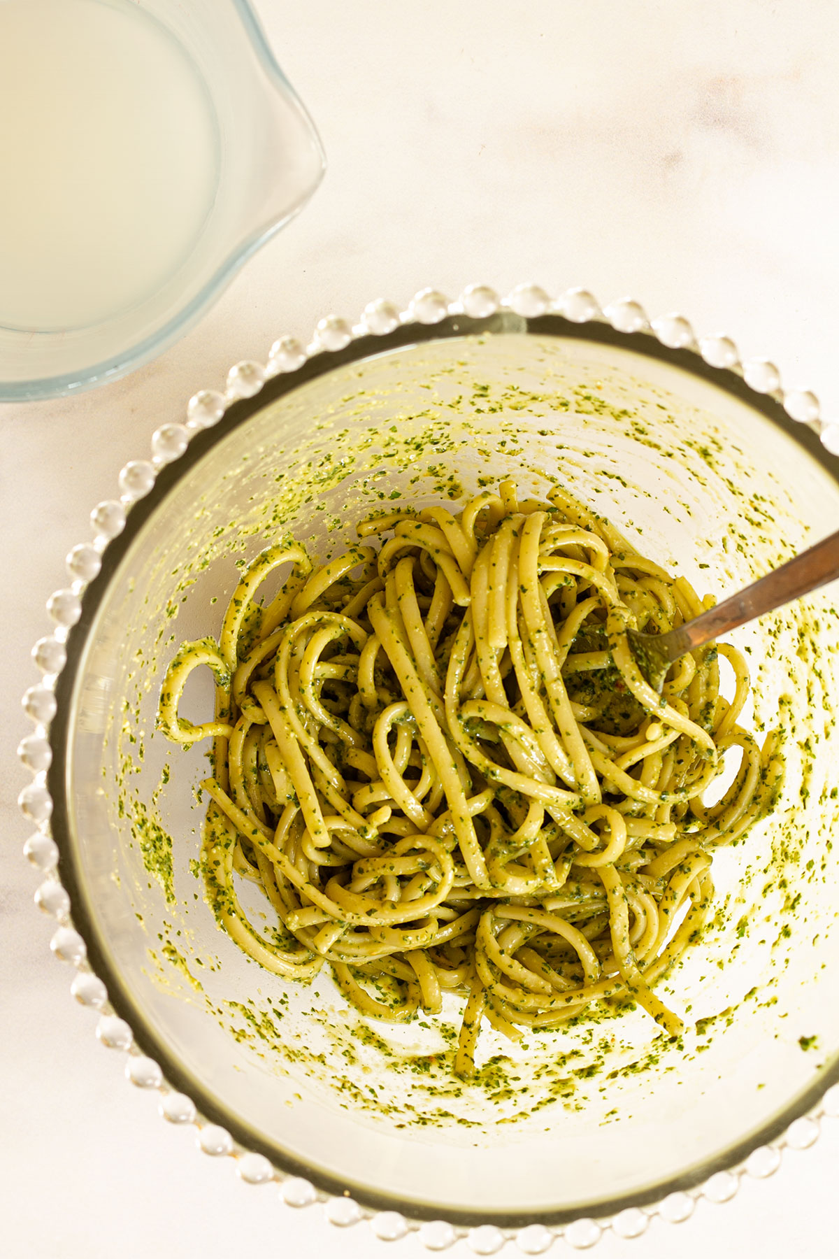 Cooked drained pasta with pesto added, in a glass bowl.