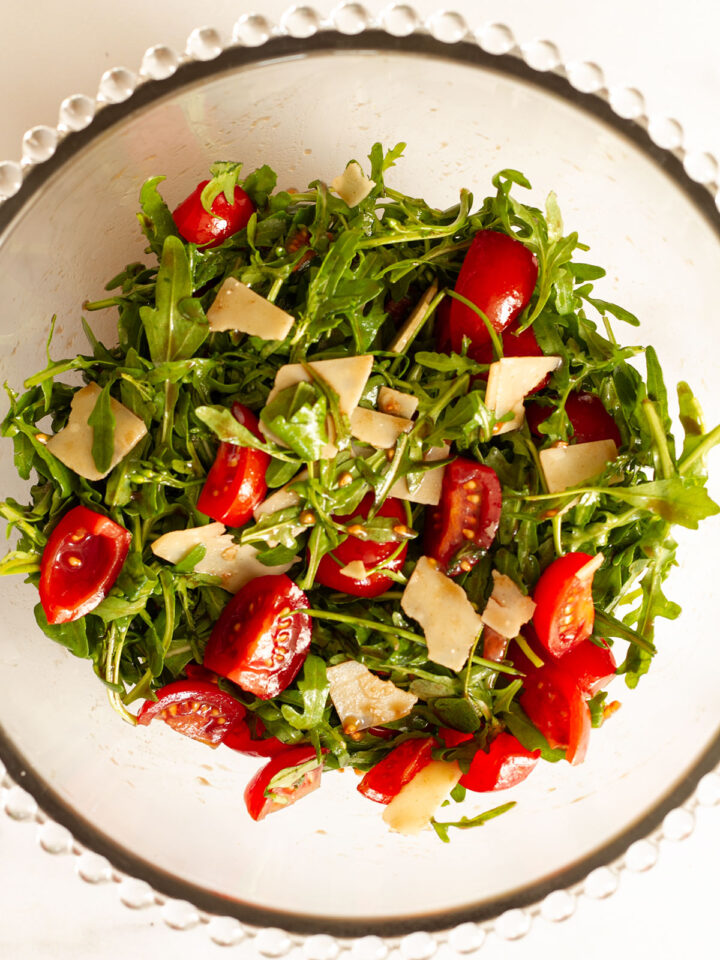 Rocket salad with tomatoes and Parmesan shavings in a glass bowl.