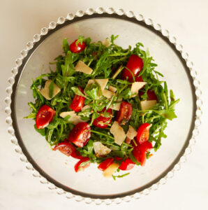 Rocket salad with tomatoes and Parmesan shavings in a glass bowl.