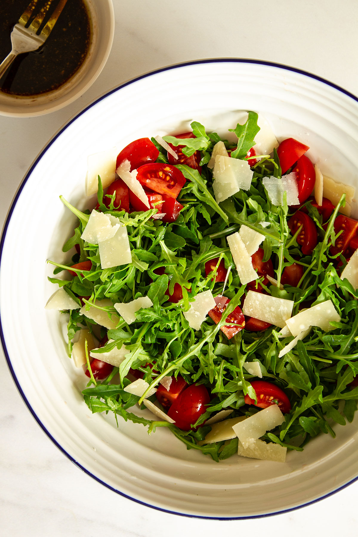 Rocket salad with tomatoes and Parmesan shavings in a white bowl.