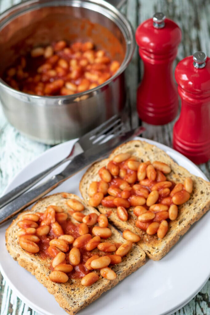 Two slices of toast topped with homemade baked beans on a white plate.