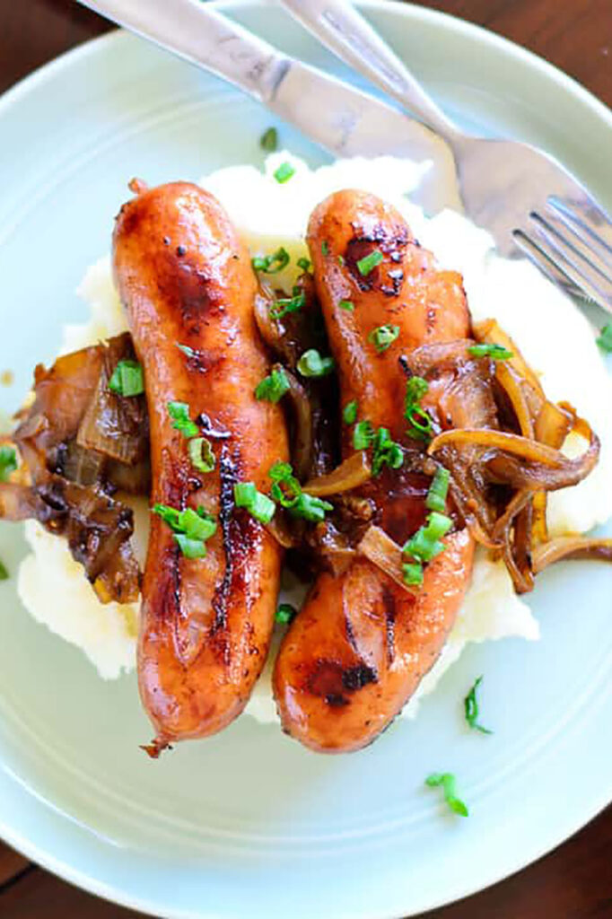 Two sausages on mash garnished with spring onions.