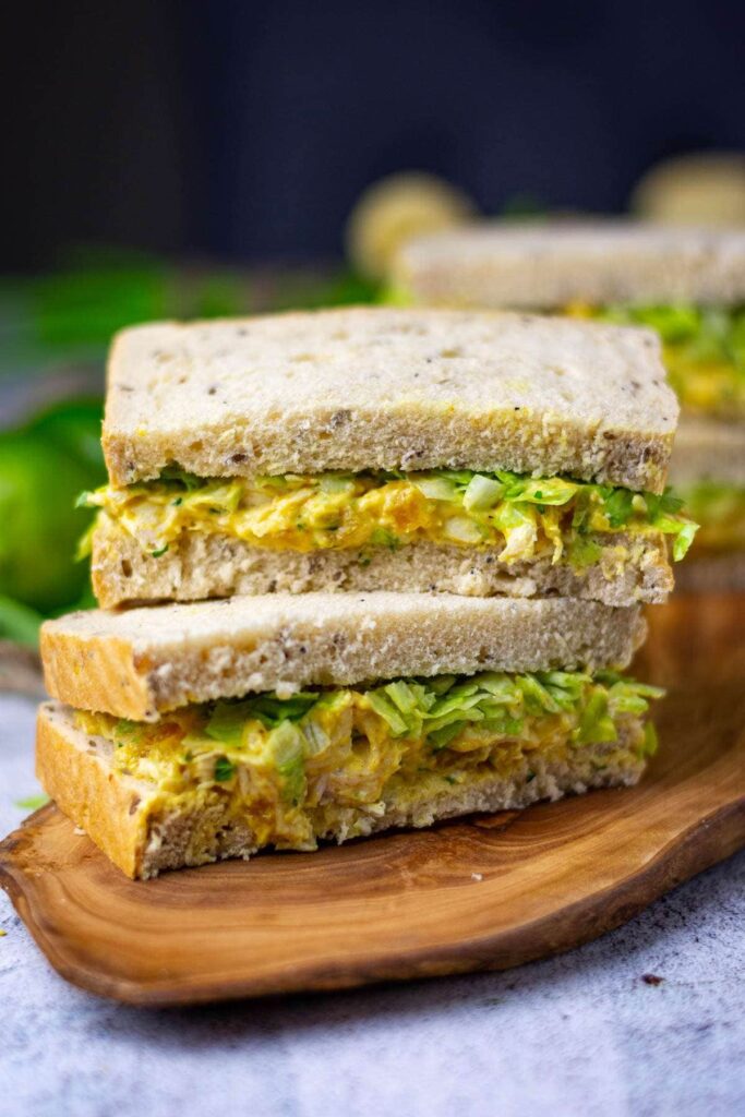 Two coronation chicken sandwiches on a wooden board.