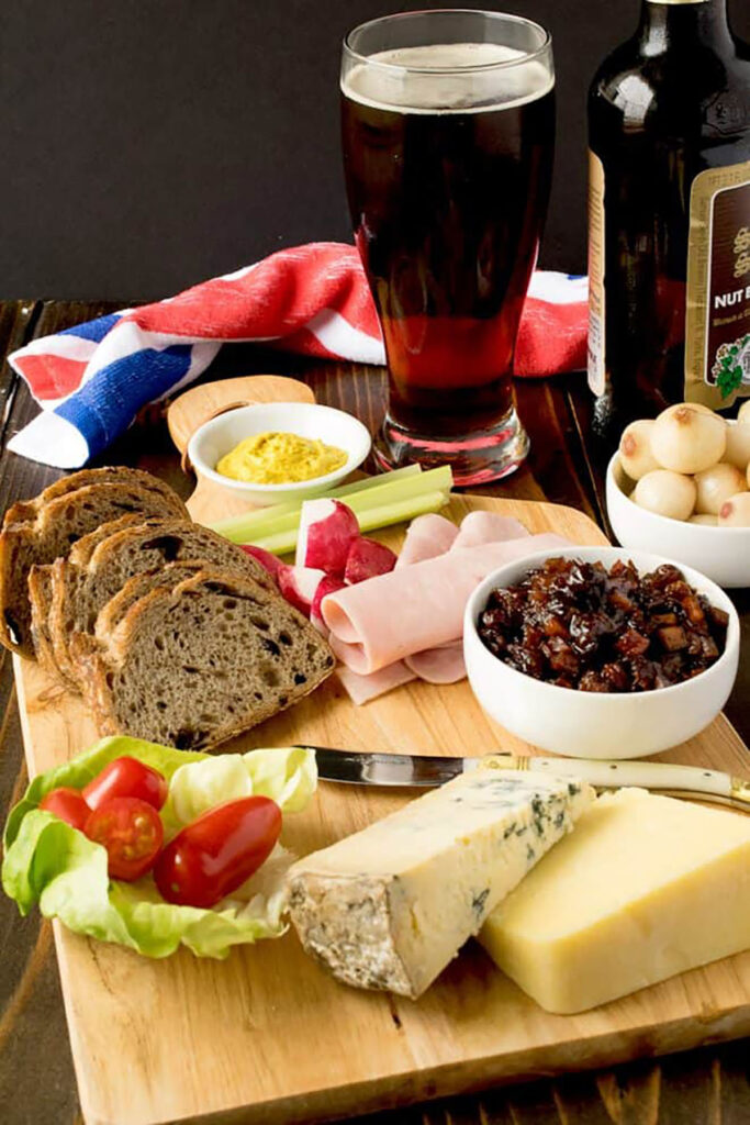 A ploughmans board with cheese, ham, bread, pickle and salad.