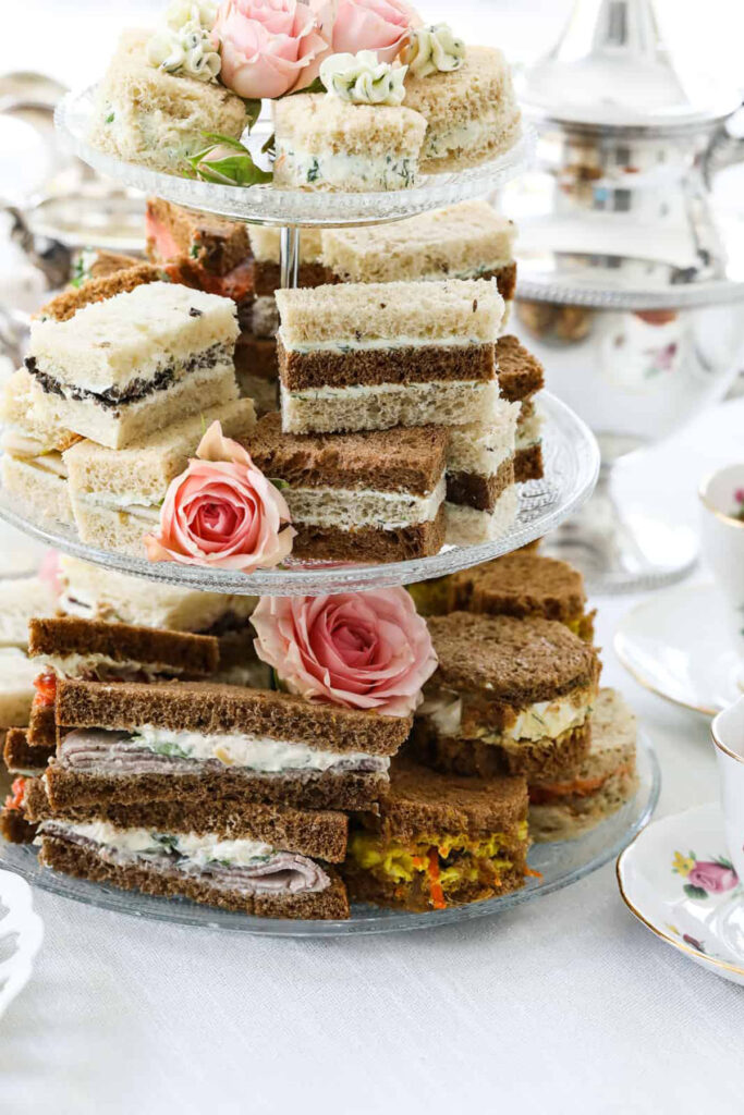 A 3 tiered stand filled with tea sandwiches decorated with pink roses.