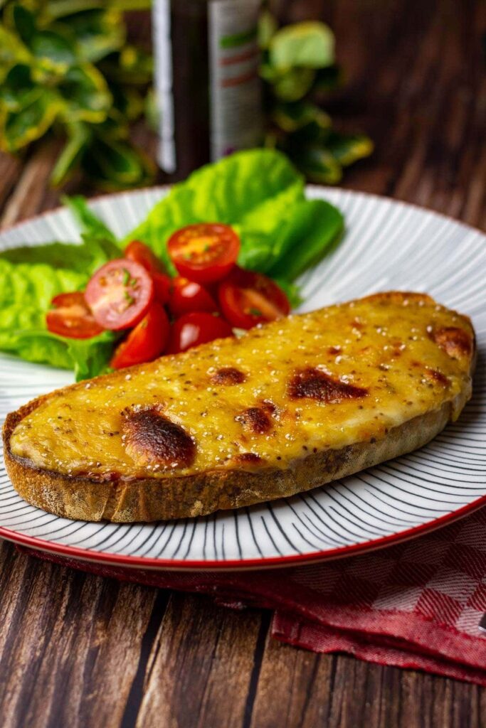 A slice of toast topped with melted cheese on a plate with salad.