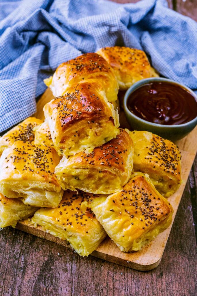 Cheese and onion rolls on a wooden board with a bowl of sauce.