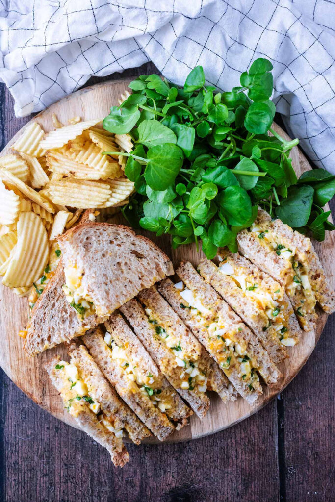 Egg and cress sandwiches on a wooded board served with crisps and salad.