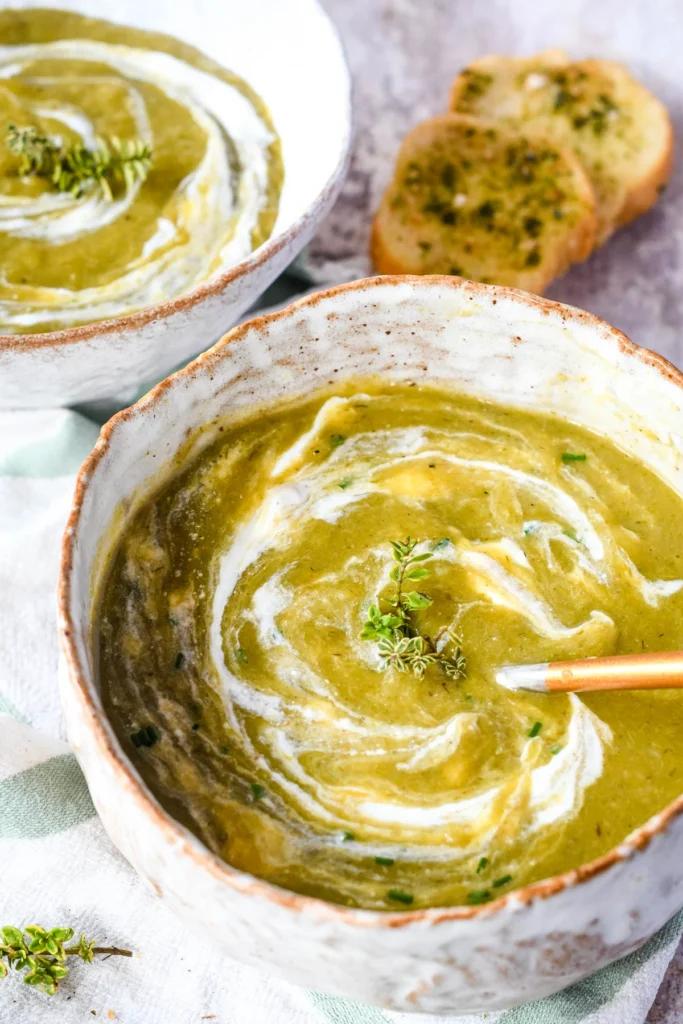 2 bowls of leek and potato soup with bread in the background.