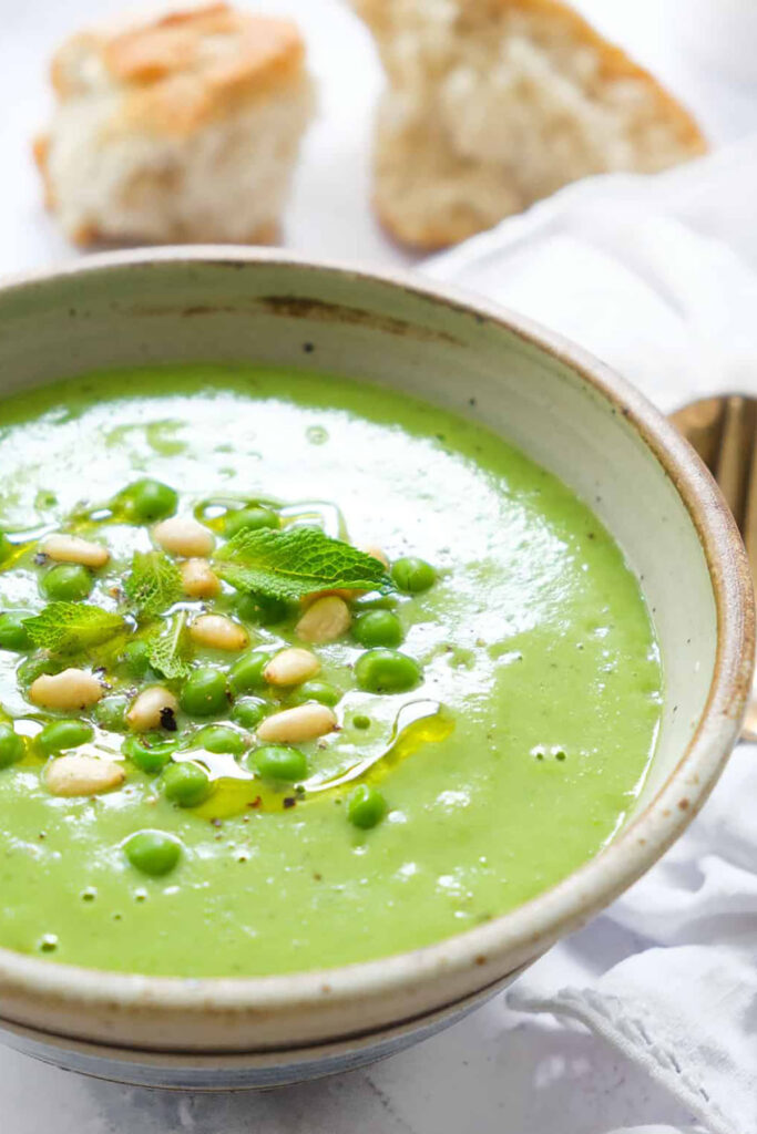 A bowl of pea and mint soup with bread in the background.